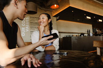 Woman smiling and listening to man holding phone and talking while they sit at table
