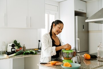 Woman smiling and squeezing orange in juicer while standing at table