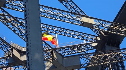 Sydney Harbour Bridge engineering framing the flying Aboriginal flag, representing Indigenous Australian heritage, culture, and national identity against bright blue sky