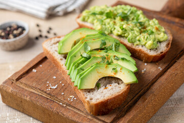 Sourdough bread toast with avocado slices, cilantro and pepper seasoning on a wooden serving board