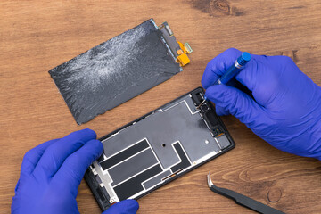 Close-up of the hands of a repairman repairing a phone display with a screwdriver
