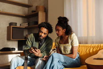 Male musician showing phone to female musician while they are sitting on couch