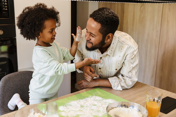 Daughter smears flour on her father's face while they stand at the table