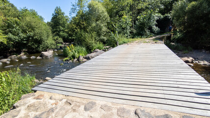 pathway wooden footbridge crossing a flowing river with rocks and green vegetation
