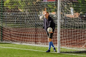 Male goalkeeper holds ball in hand and steps out of goal