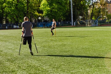 Obraz premium Male player watches ball in front of male player catching it while they lean on crutches