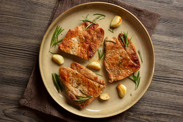 Grilled pork steak on plate on brown wooden background.