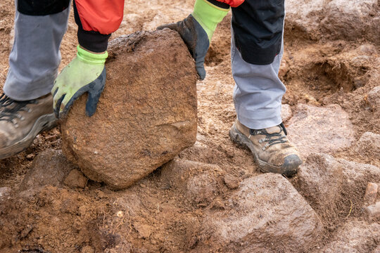 A construction worker lifting a heavy stone with gloved hands.