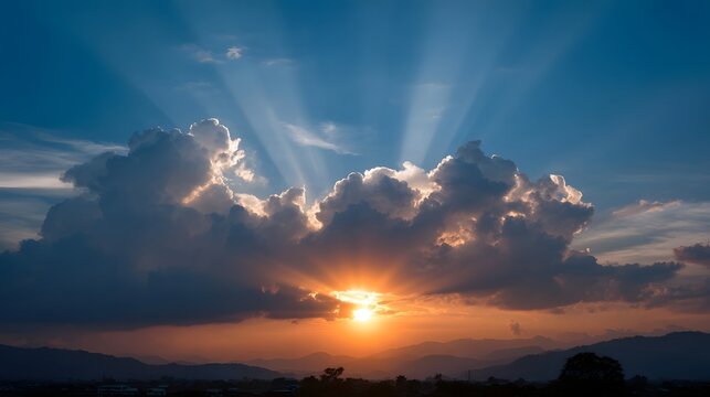 Dramatic golden sun rays emerge from behind clouds at sunset illuminating the sky and distant mountains