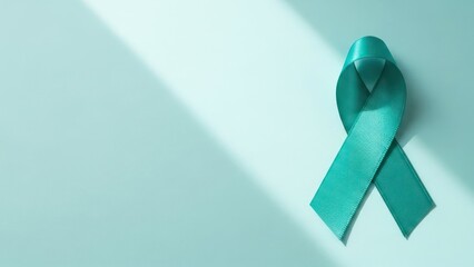 Teal awareness ribbon with natural light shadows on a light teal background