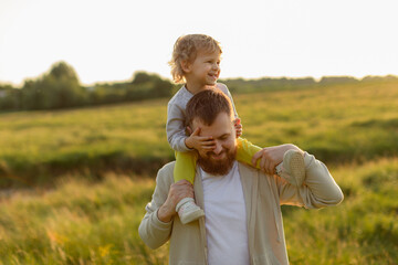 Joyful moment of a father carrying his smiling child on his shoulders during a sunny golden-hour walk. Warm light, natural emotion, and outdoor family lifestyle.