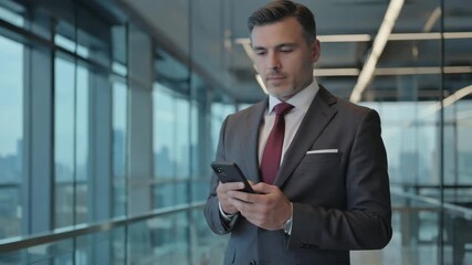 Business professional checking phone in sleek office corridor surrounded by tall glass windows