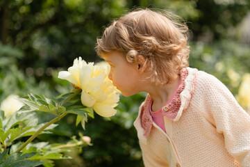 Toddler smelling a yellow flower in a sunny garden, enjoying a calm and natural moment. Soft light, warm colors, and a peaceful outdoor childhood scene.