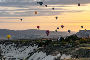 Goreme, Turkey - 19 April 2025: Aerial view of hot air balloons rising over the sculpted rock formations of Cappadocia at dawn, a symphony of vibrant colors against the pastel sky.