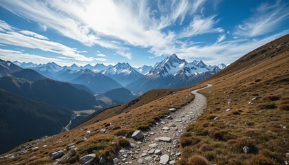 Serene mountain landscape with winding hiking trail leading toward snow-capped peaks beneath vibrant blue sky and drifting white clouds