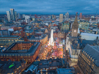 Obraz premium Aerial dusk view of Manchester skyline with Albert Square Christmas market, bright wheel and glowing festive winter streets.