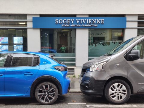 Paris, France - October 02, 2025: Blue hatchback parked beside gray van in front of Sogey Vivienne office building, showcasing urban street scene with modern vehicles. for editorial use