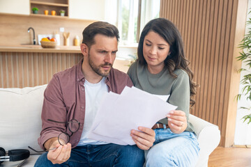 Worried couple reviewing bills and startup financial report, planning tax payments, discussing budget challenges and searching solutions together for money management during economic uncertainty
