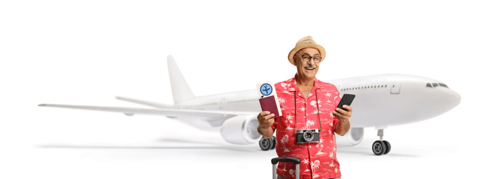 Mature male tourist holding a passport and a plane ticket and using a smartphone at the airport