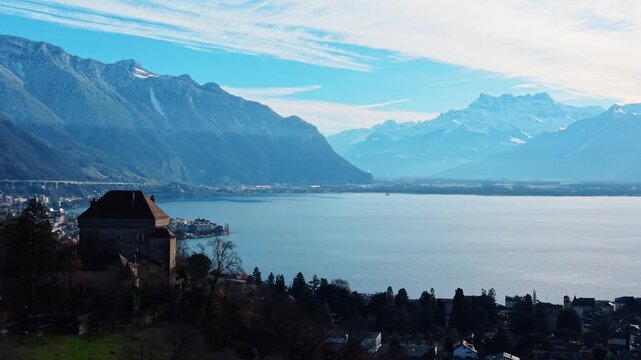 Aerial view of Chatelard Castle with its russet roof standing out against the backdrop of snow-capped mountains and tranquil lake waters, Montreux, Vaud, Switzerland.