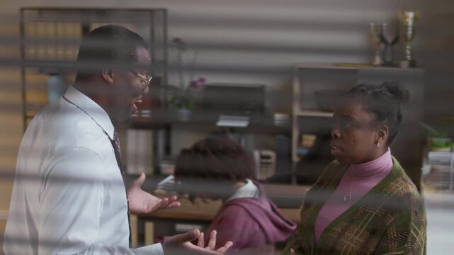 Medium shot of male black principal in formalwear discussing teenage students misbehavior with her mother during appointment in school office