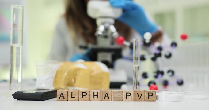 Wooden blocks spell words Alpha PVP against drug packets with tubes and microscope. Woman scientist studies synthetic stimulant risk recording data
