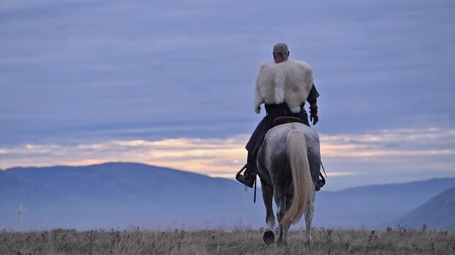 Elderly Viking warrior in fur cloak riding gray horse across open field at sunrise, mountains and distant cross behind him, moody cinematic Norse atmosphere cinematic slow motion 