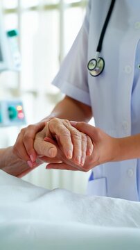 Close-up hands of caring nurse or doctor gently holding the palm of an elderly patient in a hospital setting. The health professional arms convey comfort, empathy, and support over clinical background