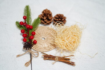 Natural decorative elements including pine cones, berries, woven mat, straw, twigs on textured white fabric for seasonal crafting and decor ideas