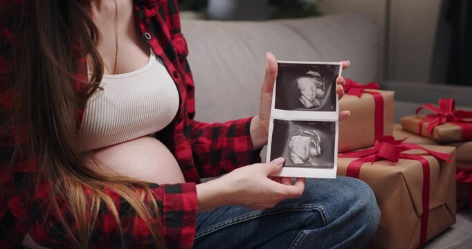 A pregnant woman holds an ultrasound image, surrounded by wrapped gifts, anticipating the arrival of her baby. Christmas Gifts and Baby Booties