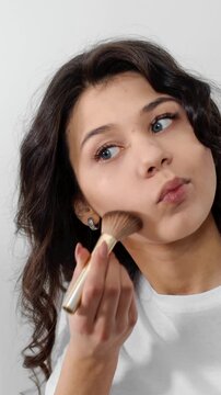 A woman applies makeup in a bright space with simple tools and focus on her look
