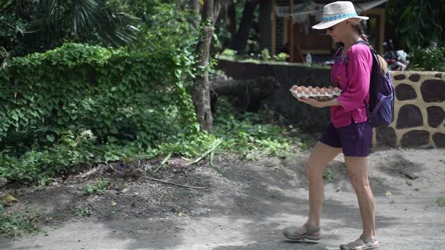 Mature woman traveler walks along the road with a basket of eggs after visiting a village market in Nicaragua.