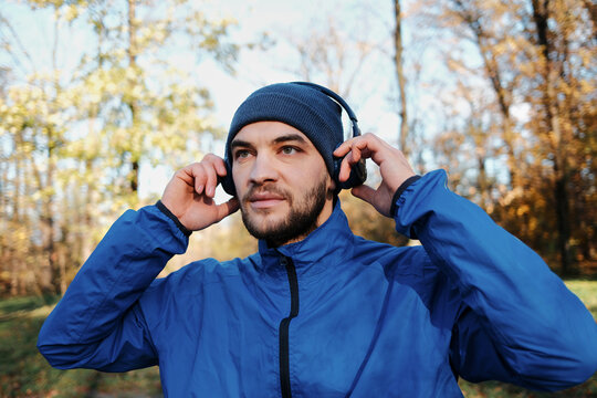 A man adjusts his headphones while standing in a forest. The scene conveys focus and a refreshing outdoor pause.