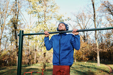 A man performs pull-ups on an outdoor bar. The action captures strength and determined physical training.