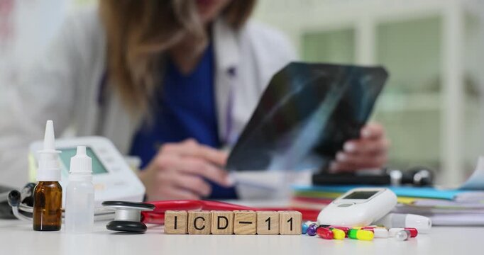 Wooden blocks spell ICD-11 near nasal spray monitor and pills on desk against doctor. Woman physician reviews x-ray updating diagnosis with ICD rules