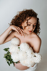 a pregnant woman with flowers on a white isolated background patting her belly and enjoying her...
