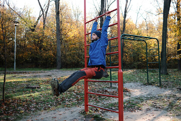Obraz premium A man performs a hanging leg raise on red outdoor bars in an autumn park. The concept expresses discipline, core strength and personal progress.