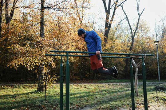 A man exercises on parallel bars in a park. The moment reflects discipline and committed outdoor training.
