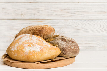 Freshly baked bread on cutting board against white wooden background. perspective view bread with copy space