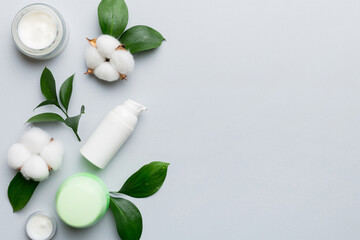Organic cosmetic products with cotton flower and green leaves on color background. Copy space, flat lay