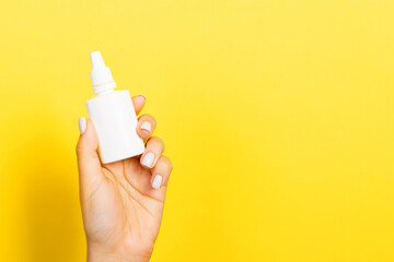 Female hands hold medicine bottle nose spray on yellow background isolation