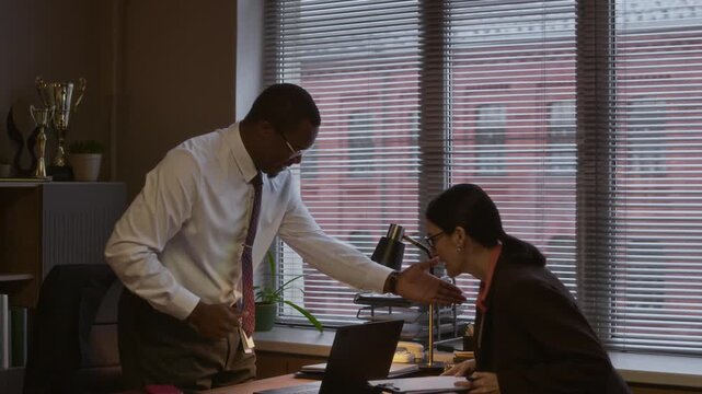 Zoom in shot of male black principal greeting female Caucasian counselor and having serious discussion in modern school office