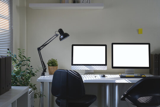 A workspace featuring a two computer monitor, desk lamp, and office supply elements