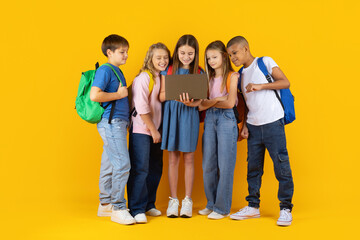 Group of preteen children gathered around a laptop in a bright studio background. Curious pupils exploring digital learning together in a modern education lifestyle scene