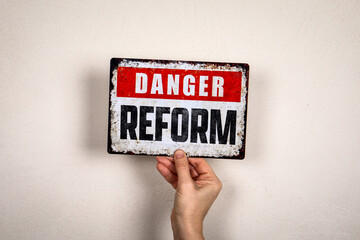 Danger Reform Warning Sign Held By Hand Against Neutral Wall Background