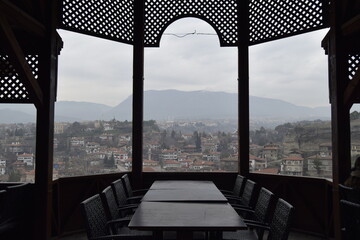 View of a serene cityscape framed by the dark, ornate woodwork of a gazebo, offering a tranquil escape above the rooftops, Karabuk, Karabuk, Turkey.