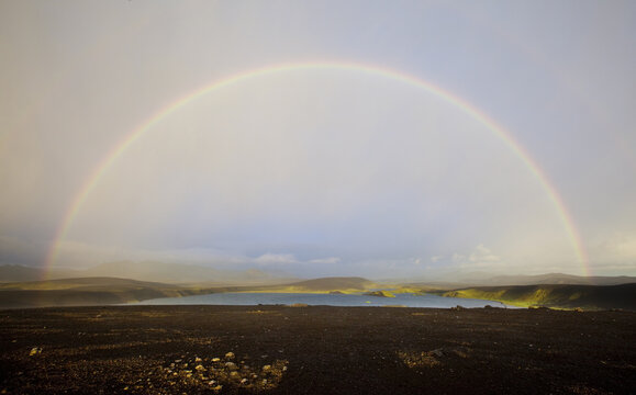 View of a vibrant rainbow arcs over a serene lake, contrasting with the dark, volcanic ground in this Icelandic landscape, Veidivotn, Rang&aacute;r&thorn;ing ytra, Iceland.