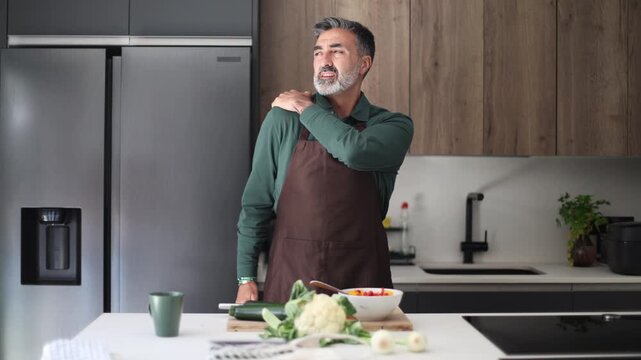 Mature man experiencing sudden shoulder pain while cooking