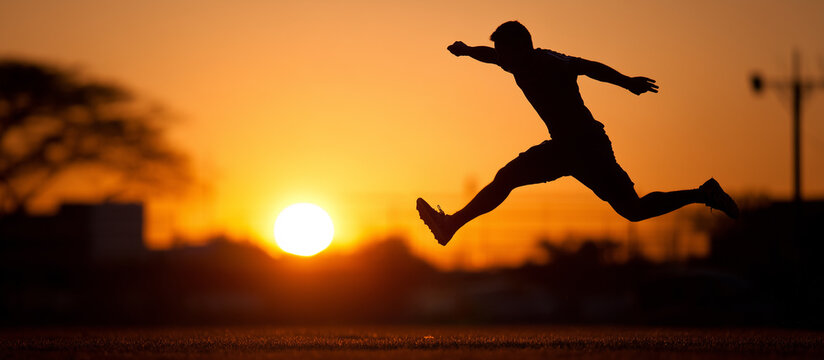 Silhouette of a man leaping in front of a vibrant sunset banner. - Powered by Adobe