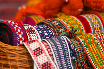 Close-up of colorful handwoven traditional belts displayed in a basket, highlighting their intricate patterns and vibrant colors.